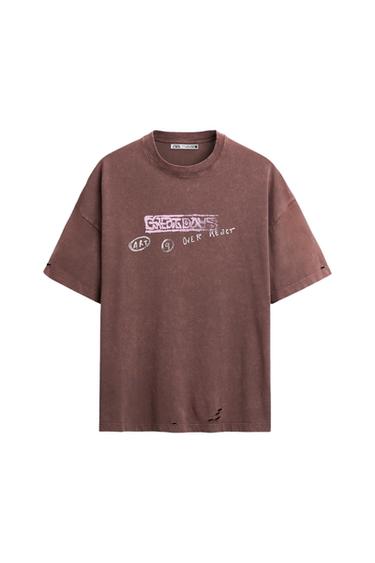 Front view of a brown t-shirt with 'OVER REACT' text, graphic and distressed details.