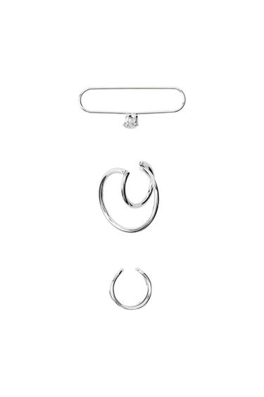 Three silver-coloured ear cuff earrings on a white background: an elongated design with a sparkling detail, a double hoop, and a single hoop.