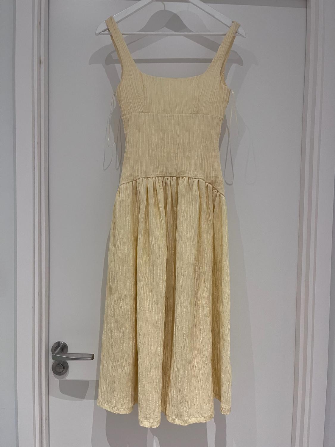 Long light-yellow dress with a crinkled texture, hanging on a hanger over a white door. Casual and relaxed style.