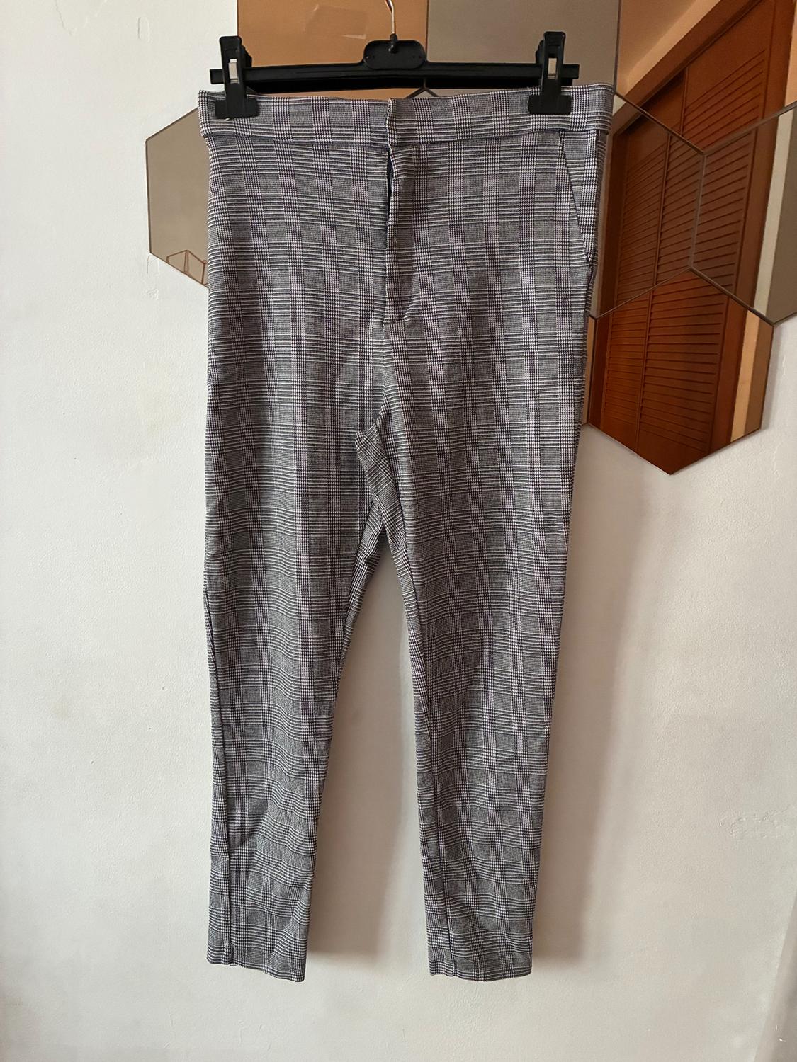 Grey checked trousers hanging on a black hanger against a white wall, reflected in a hexagonal mirror.