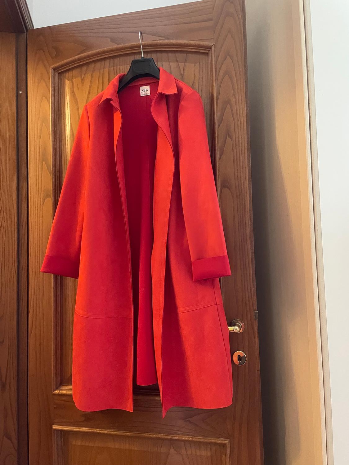 Red coat hanging on a wooden door, with a visible label on the collar.