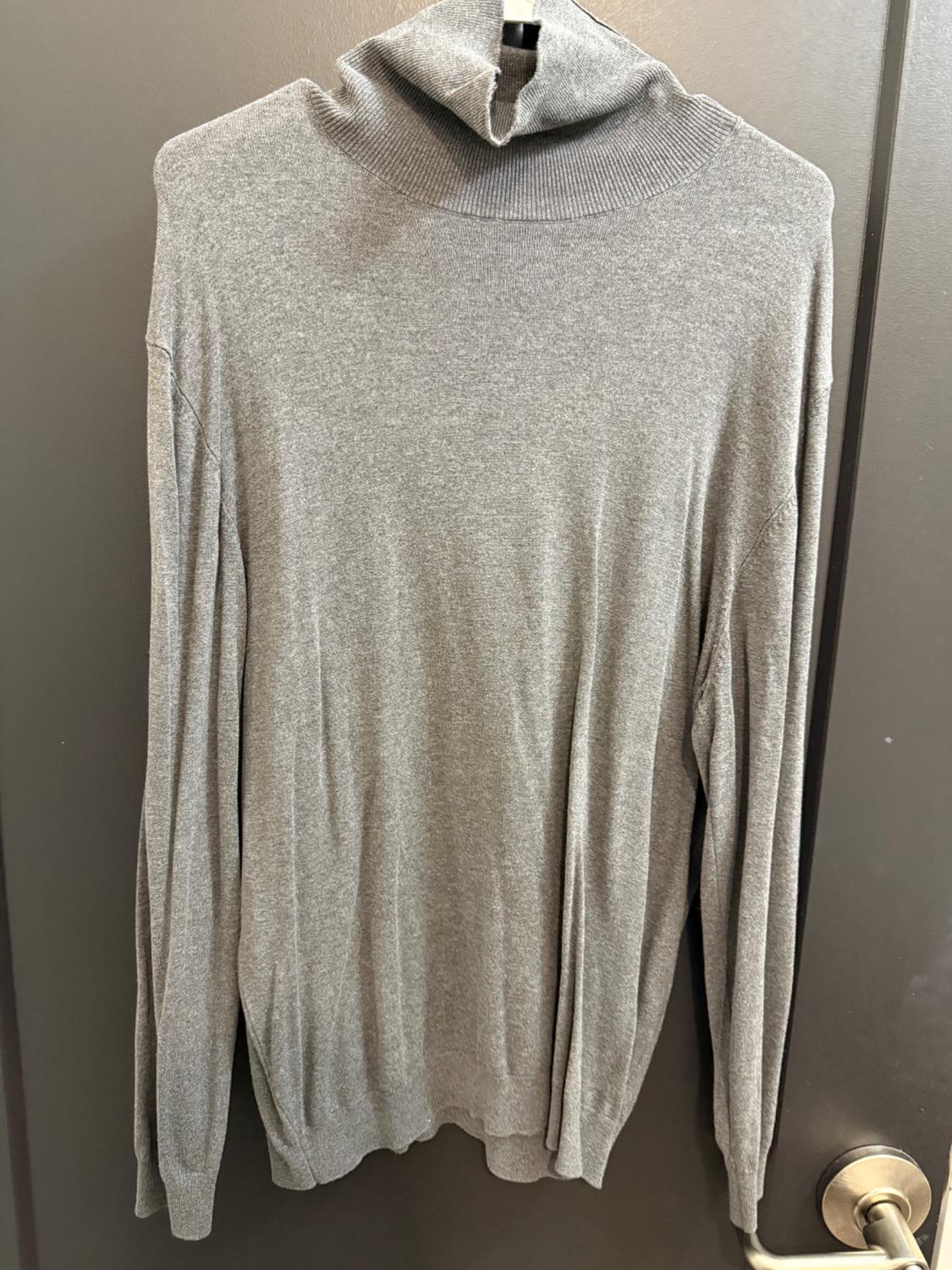 Gray turtleneck sweater hanging on a gray door. The texture of the fabric is visible, with long sleeves and a simple design.