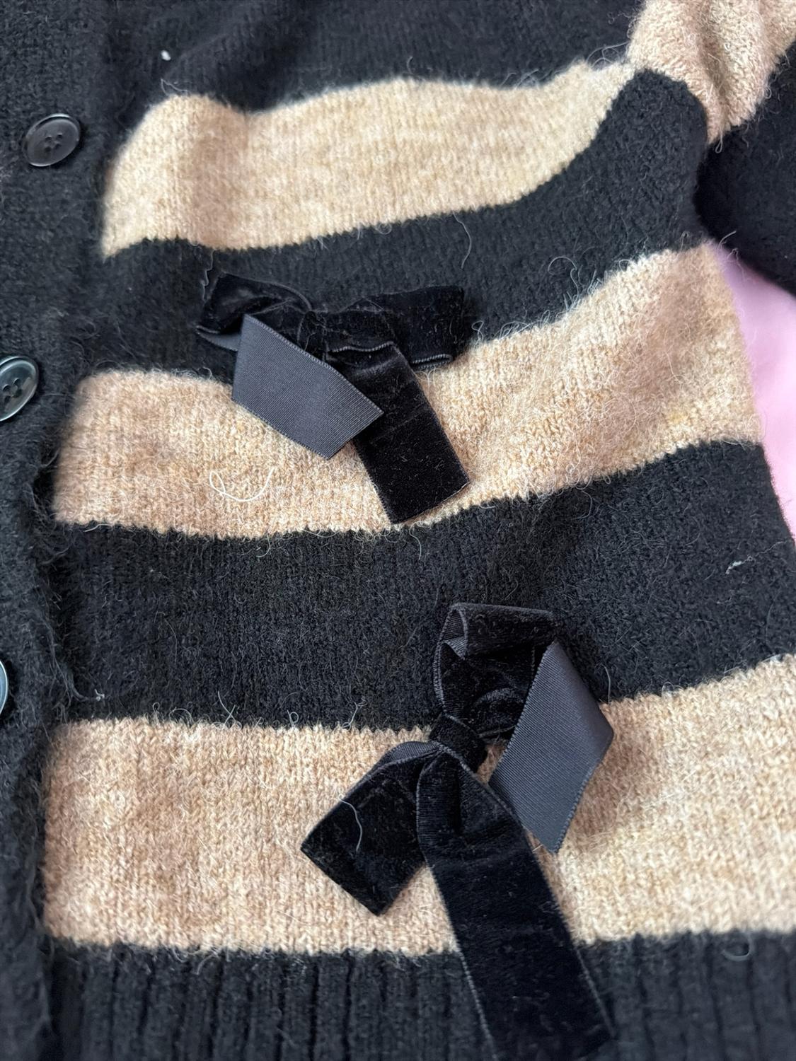 Detail of a knitted cardigan with black and beige horizontal stripes, buttons and two black velvet bows.