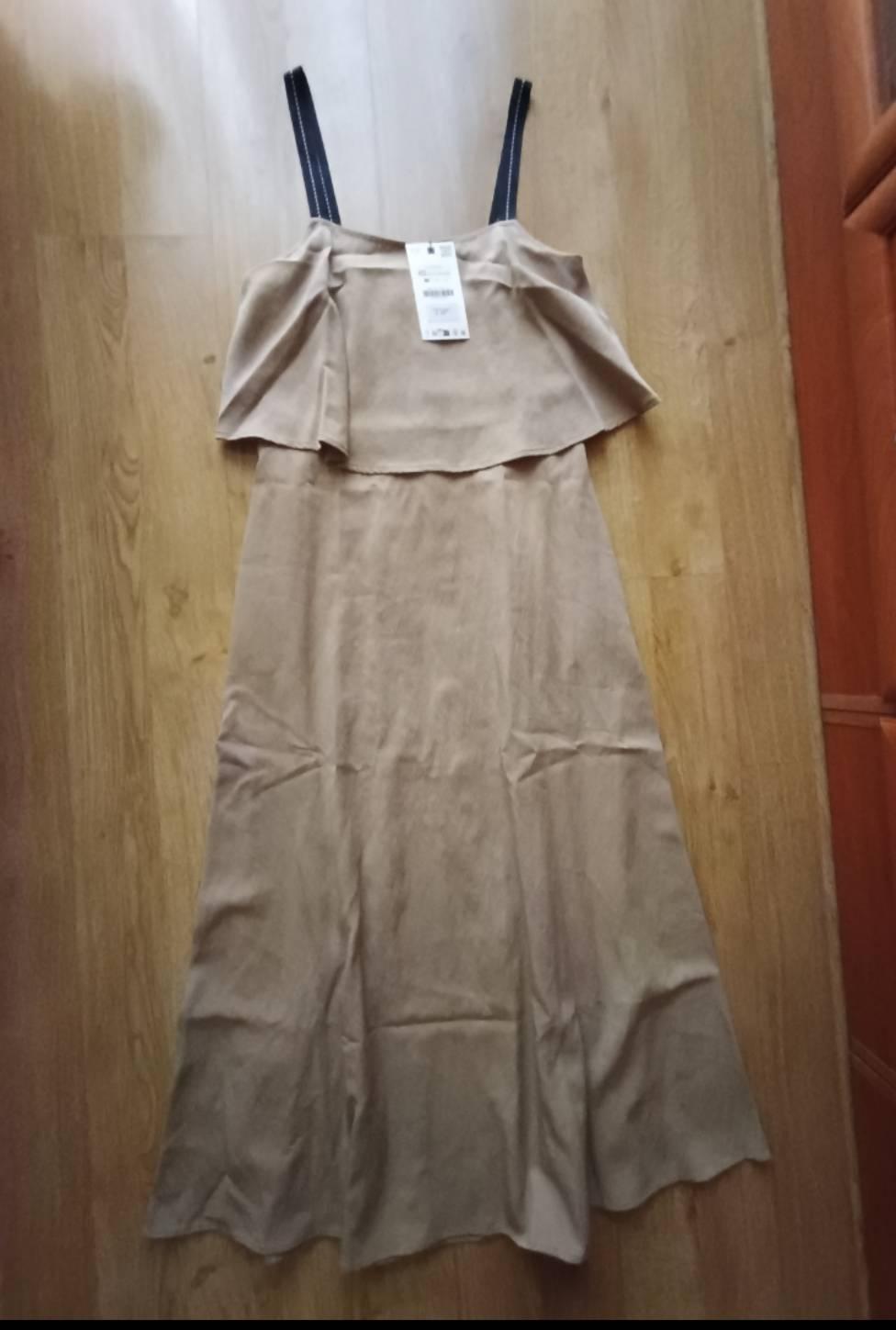 Long beige dress with black straps and a frill on the neckline, laid out on a wooden floor.