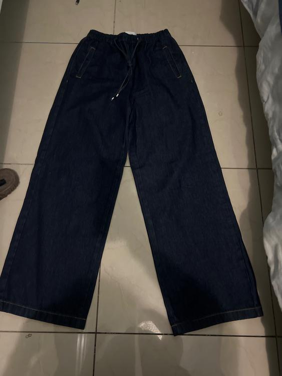 Dark blue denim wide-leg pants with an elastic waist and drawstring, placed on a light tiled floor.