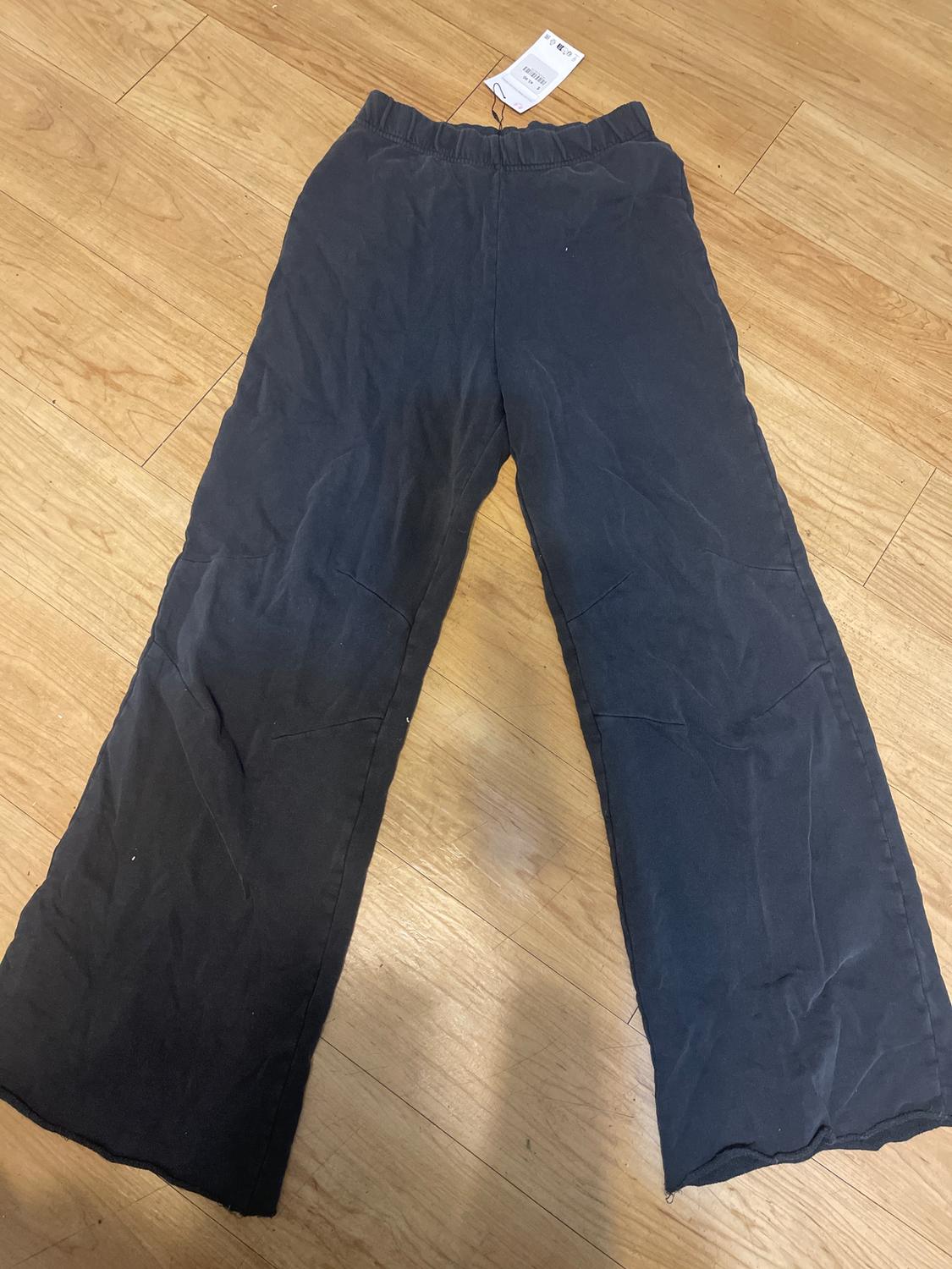 Black wide-leg pants with an elastic waist, laid on a light wooden floor. Visible tag on the upper part.