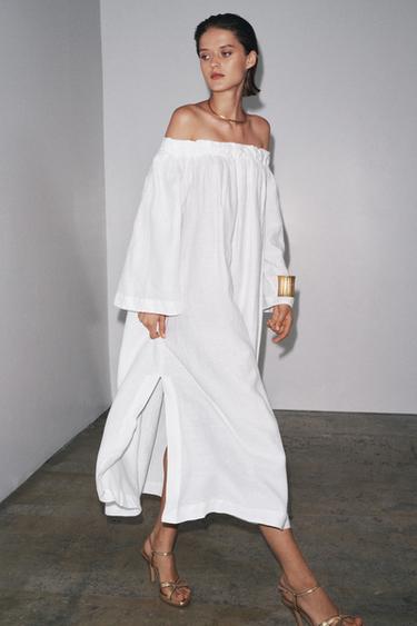 Komplet dlouhých bílých šatů s elastickým rovným výstřihem, dlouhými rukávy a bočním rozparkem ve spodní části.