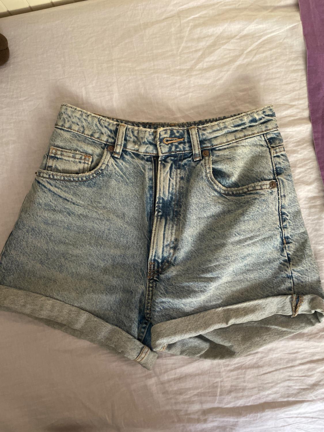 Light blue denim shorts with rolled hems, placed on a bed with white and purple sheets.