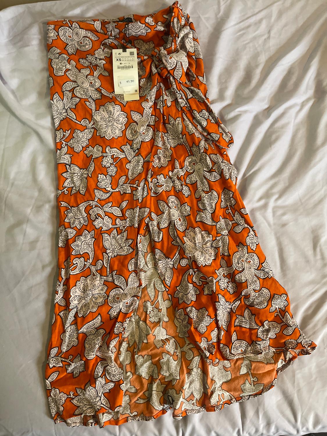 Orange dress with white floral print and price tag of $45.90, size XS, on a white surface.