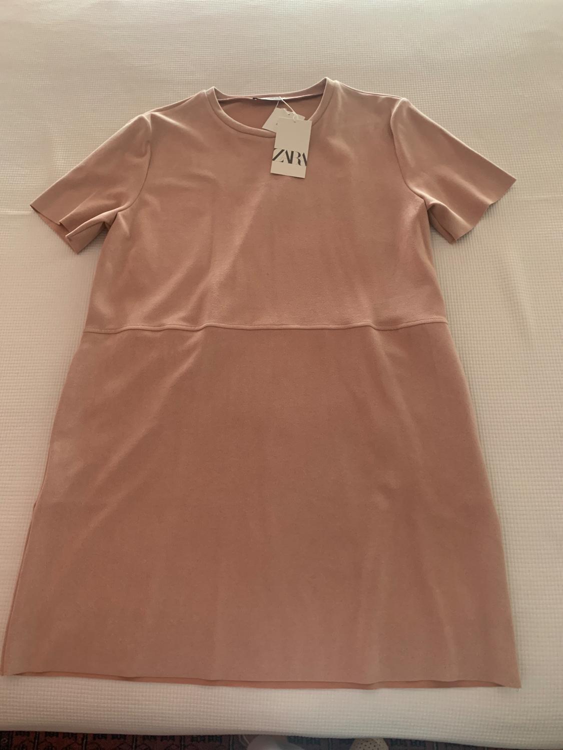 Light pink short-sleeved dress on a white surface, with a visible label that says "ZARA".