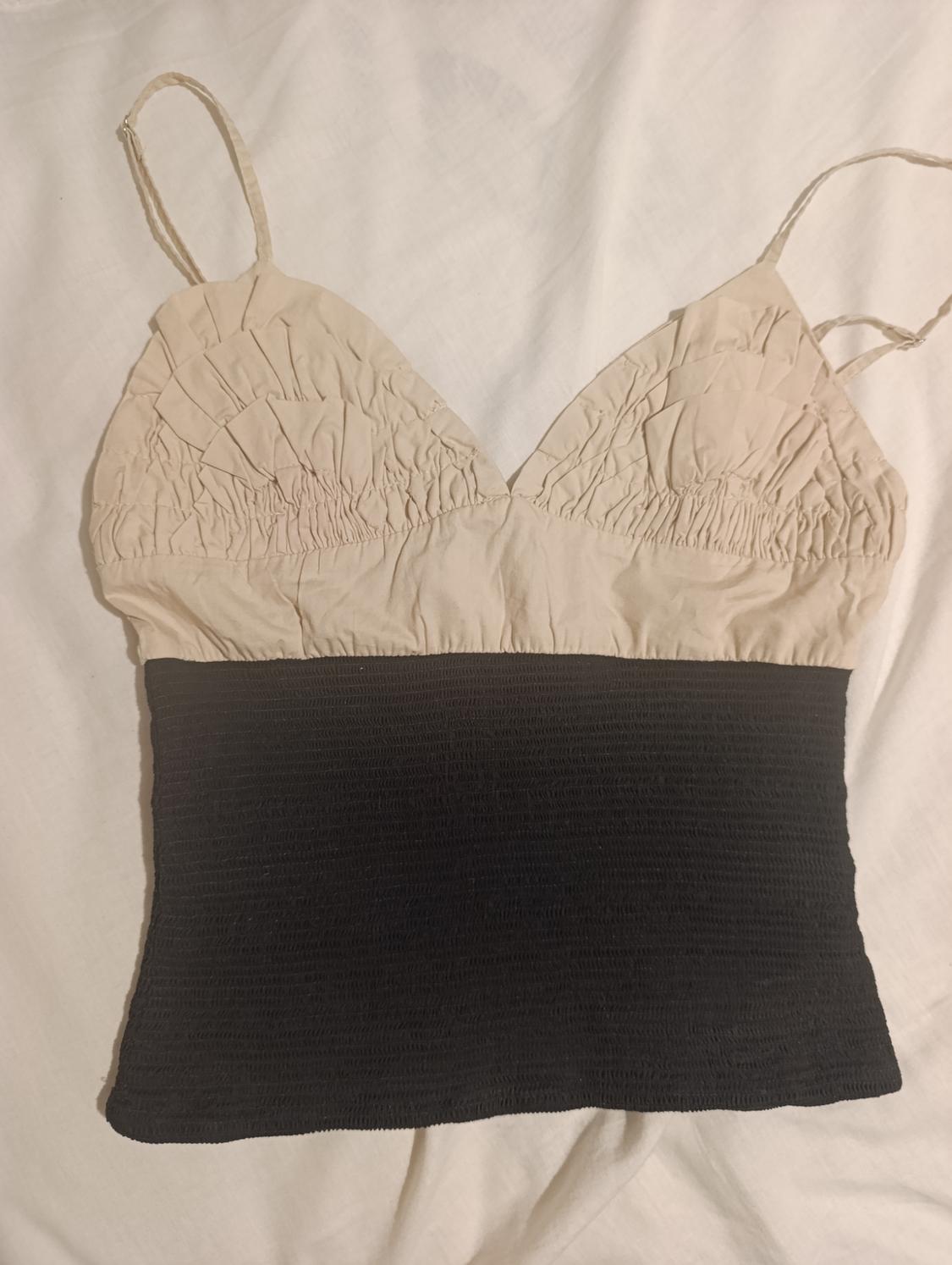 Fine-strap top with ruched beige upper part and pleated black lower part, on a white background.