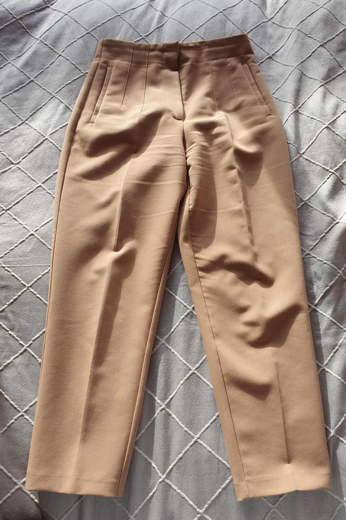 Front view of beige trousers with side pockets and vertical pleats.