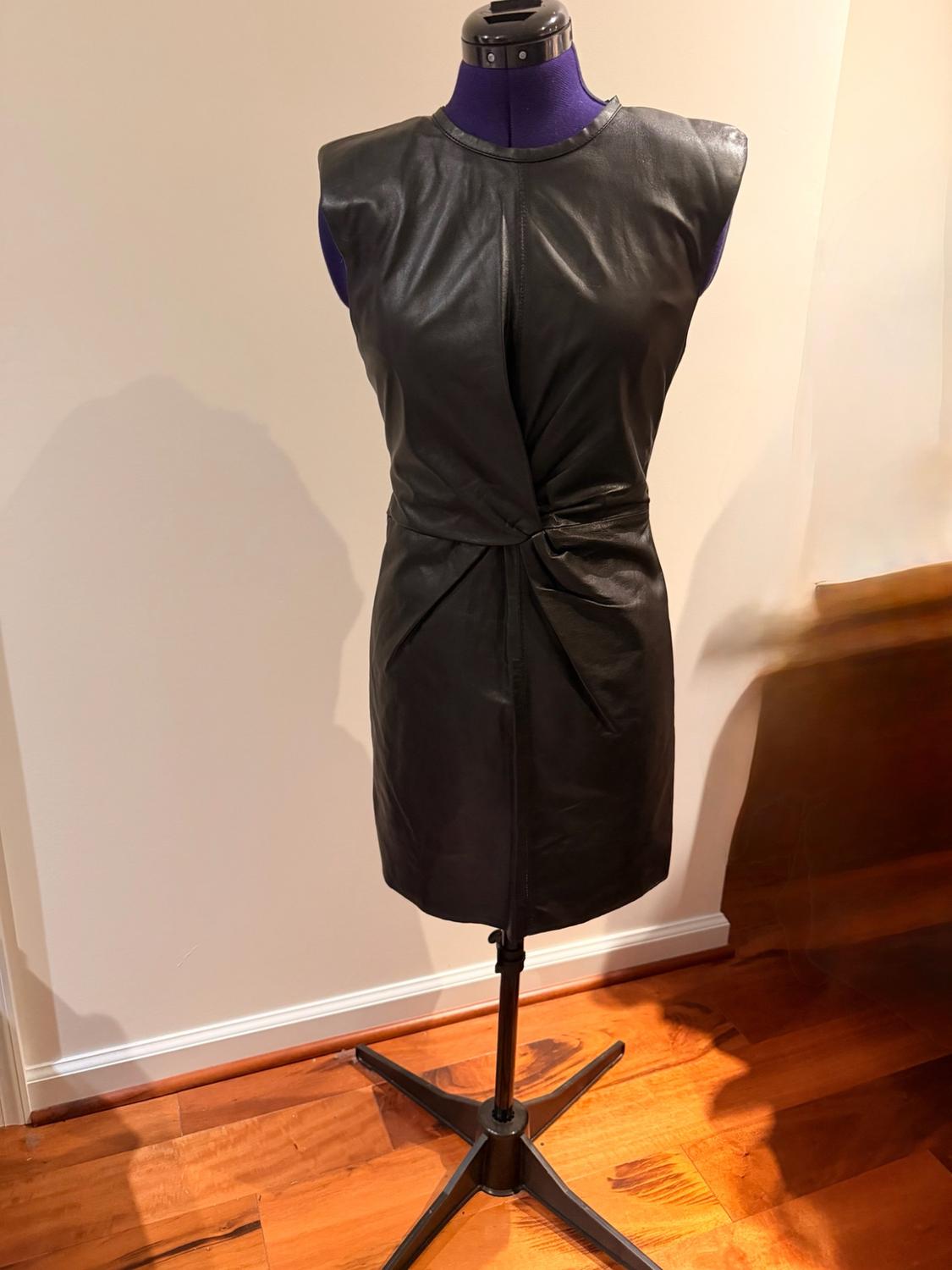 Sleeveless short black dress with a knot detail at the waist, displayed on a blue mannequin in a room with wooden flooring.