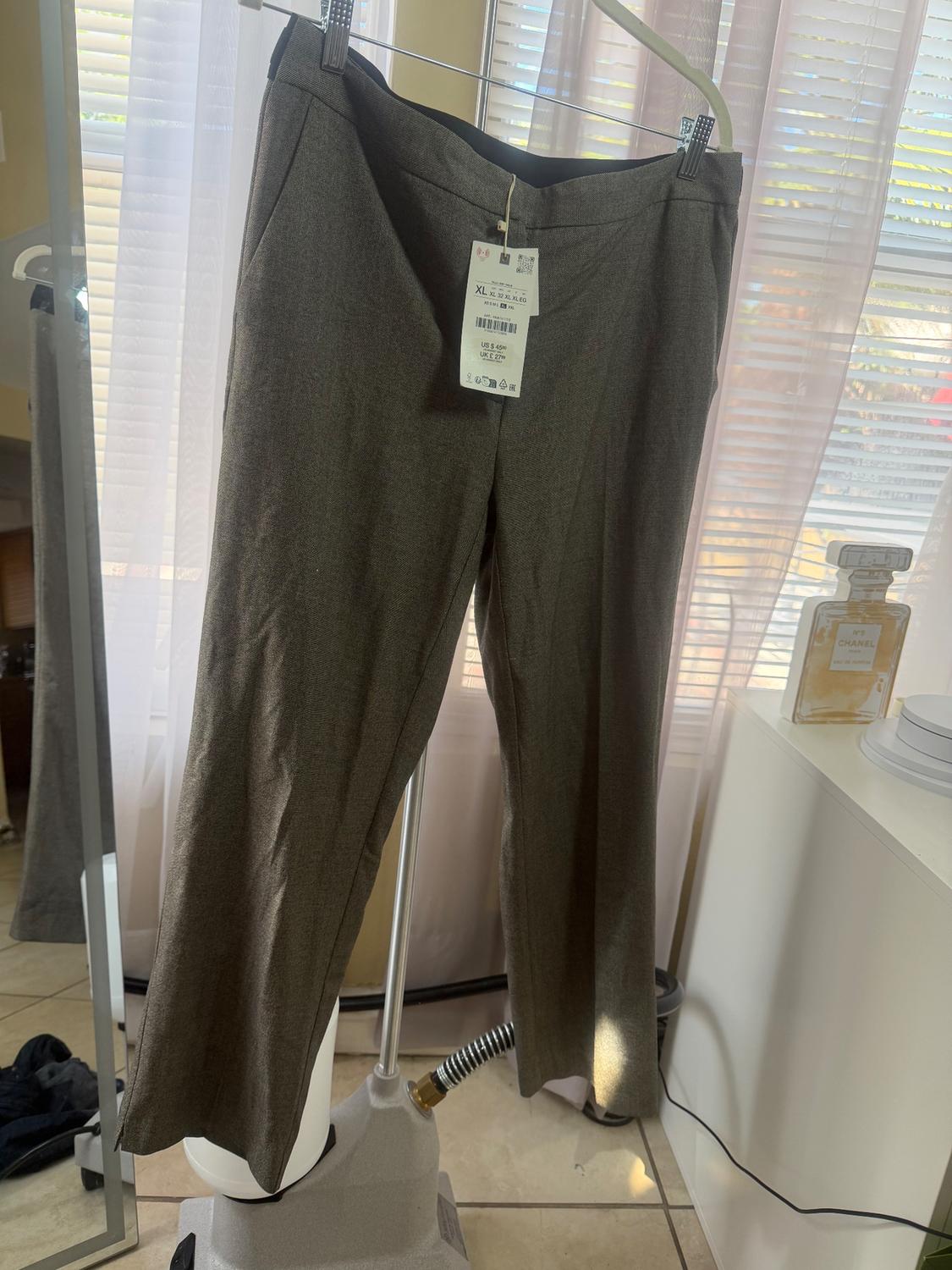 Gray pants hanging on a hanger with an XL size tag, in front of a window with white curtains and natural light.