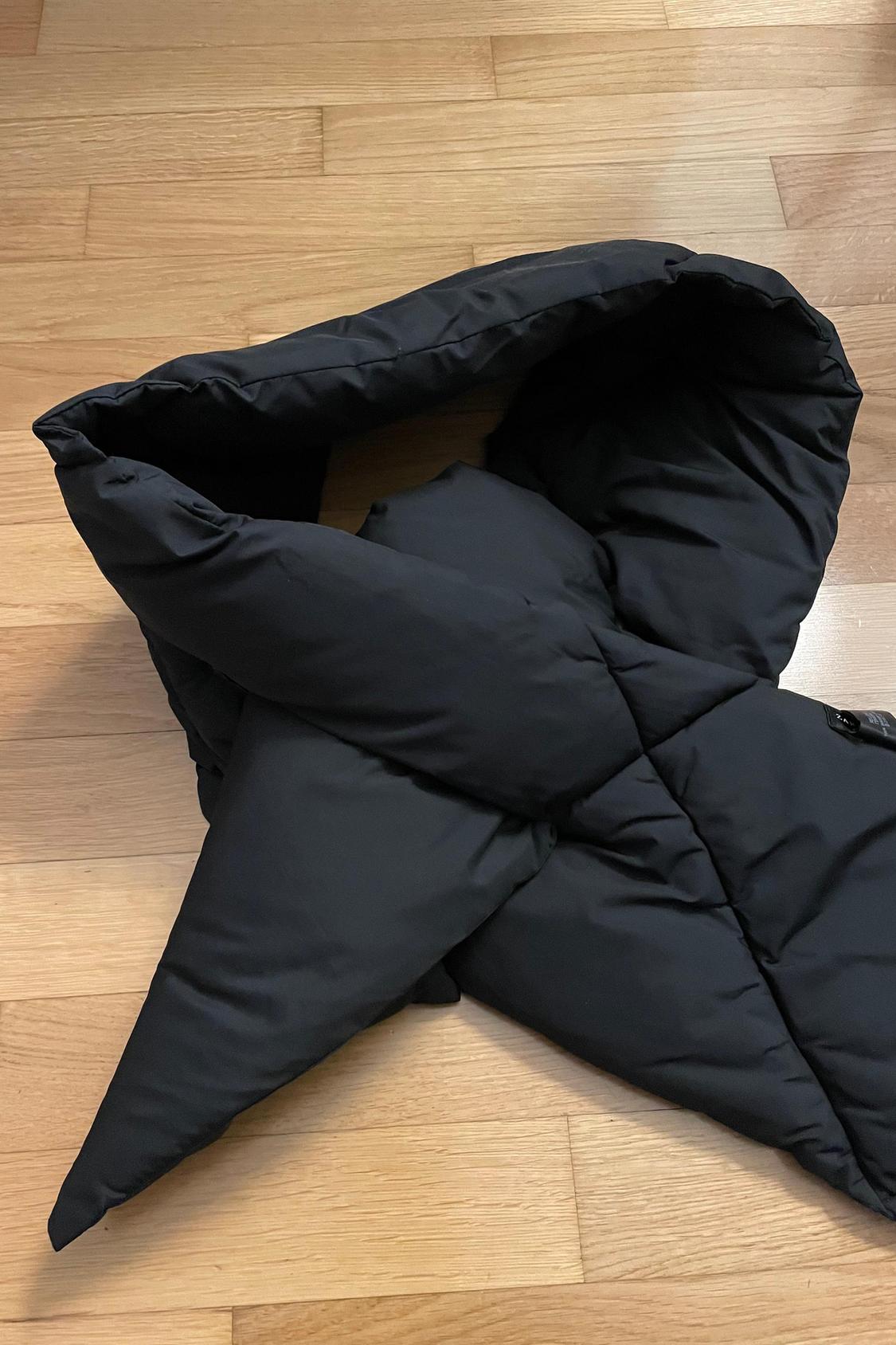 Detail of black quilted scarf on wooden floor.