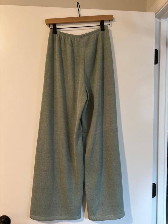 Light green wide-leg pants hanging on a wooden hanger over a white door.