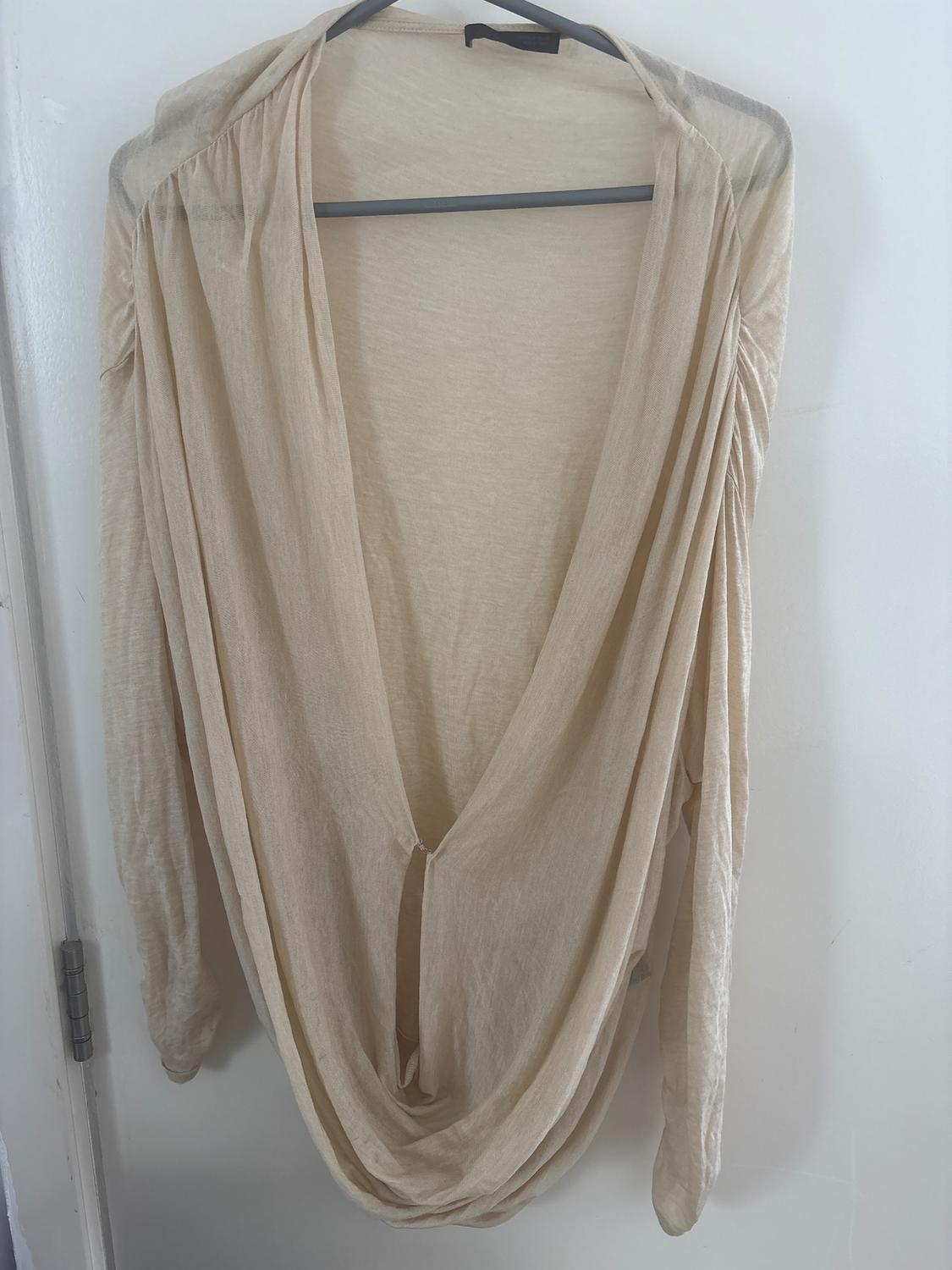 Long-sleeved beige blouse with a deep V-neck, hanging on a hanger over a white door.