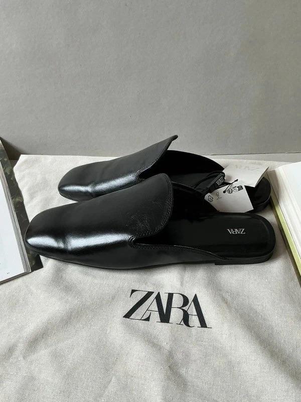 Black slingback shoes with labels on a fabric bag with the text ZARA. Relaxed composition with books at the edges.