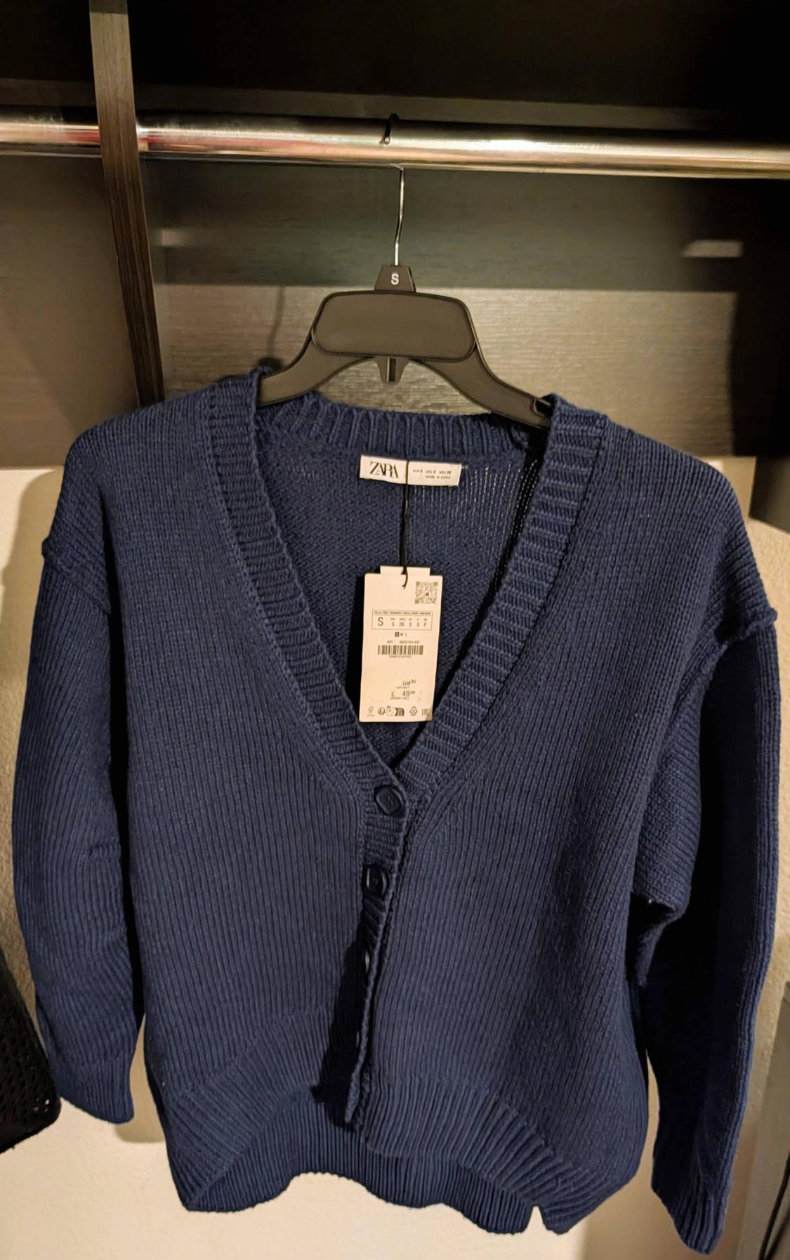 Blue cardigan hanging on a black hanger with a visible price tag. Dark closet background.
