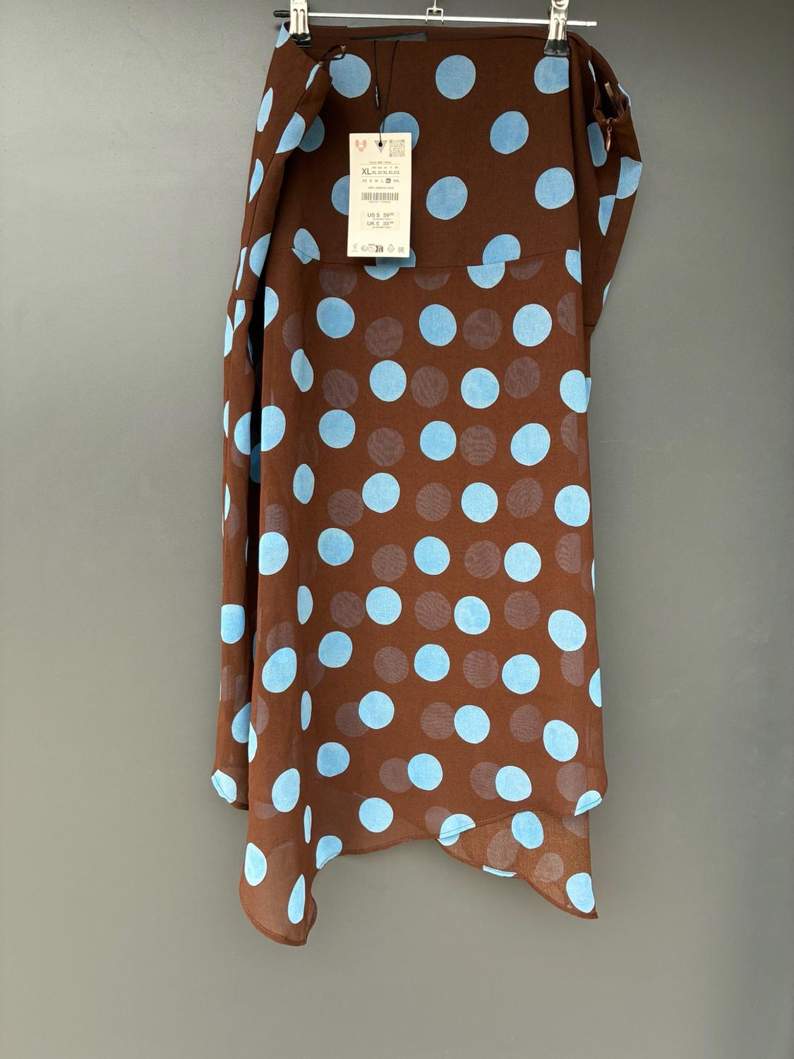 Brown skirt with light blue polka dots hanging on a hanger against a grey background. Visible label with text: XL, US $59.90, UK £35.99.