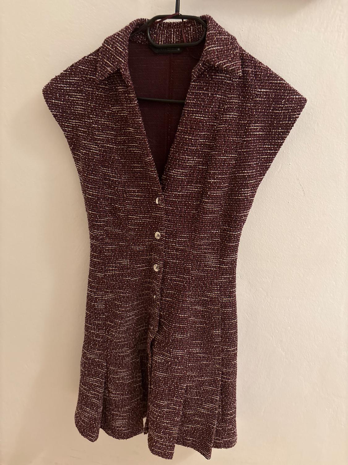 Burgundy textured sleeveless jumpsuit, hanging on a black hanger. Features front buttons and a classic collar.