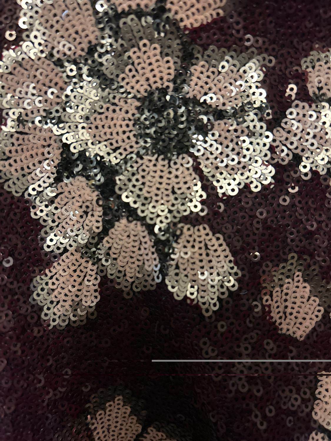 Close-up of a sequined fabric forming a floral pattern in silver and black tones on a dark background.