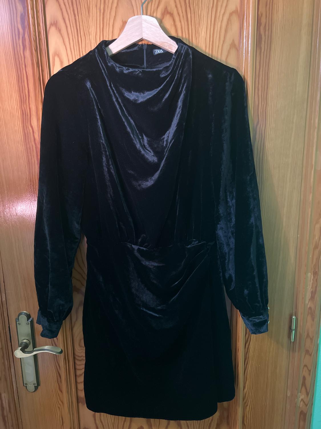 Black velvet dress with long sleeves hanging on a wooden hanger in front of a wooden door.