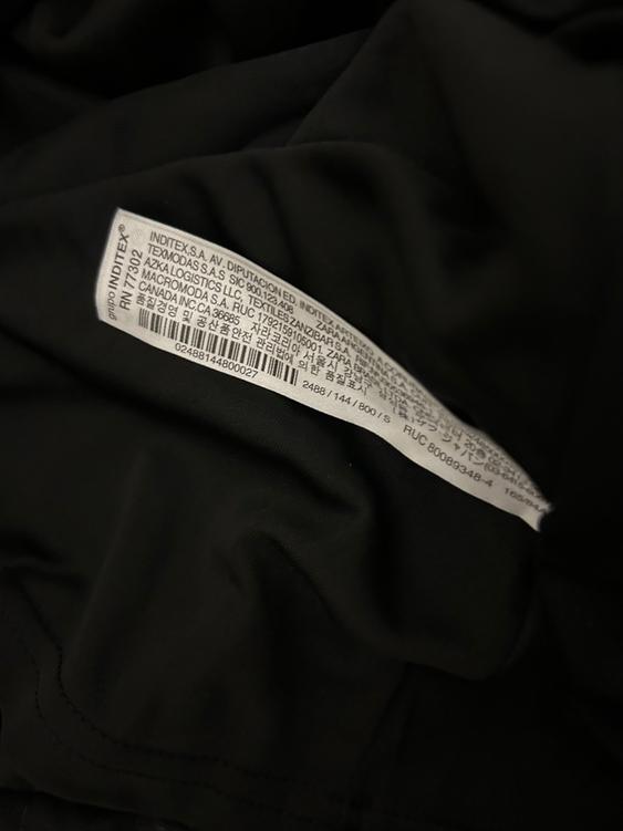 White label with multi-language text on black fabric. It reads "INDITEX S.A." and "ZARA" among other details.