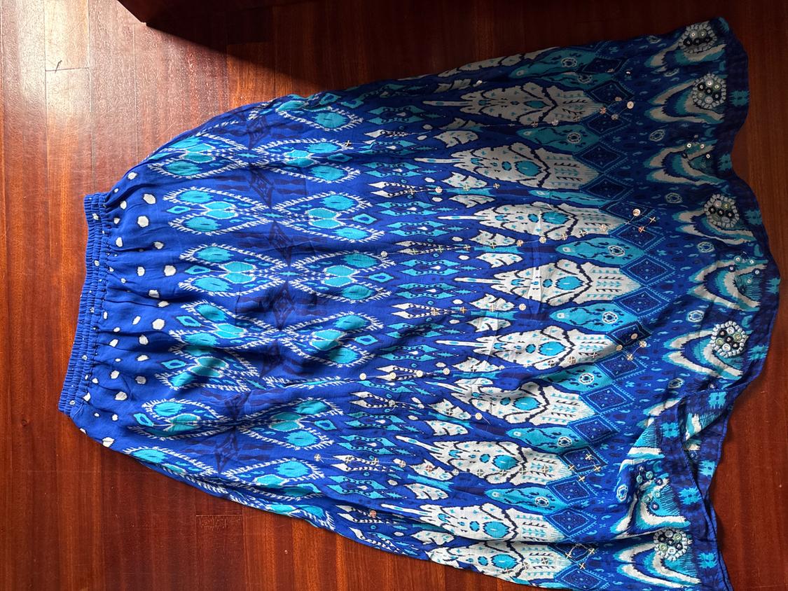 Long blue skirt with a white and light blue abstract print, elasticated waist, and sparkly details, laid out on a wooden floor.