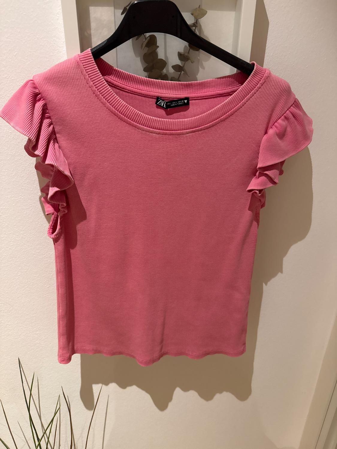 Pink t-shirt with ruffled sleeves, hanging on a black hanger. White background with decorative leaves.