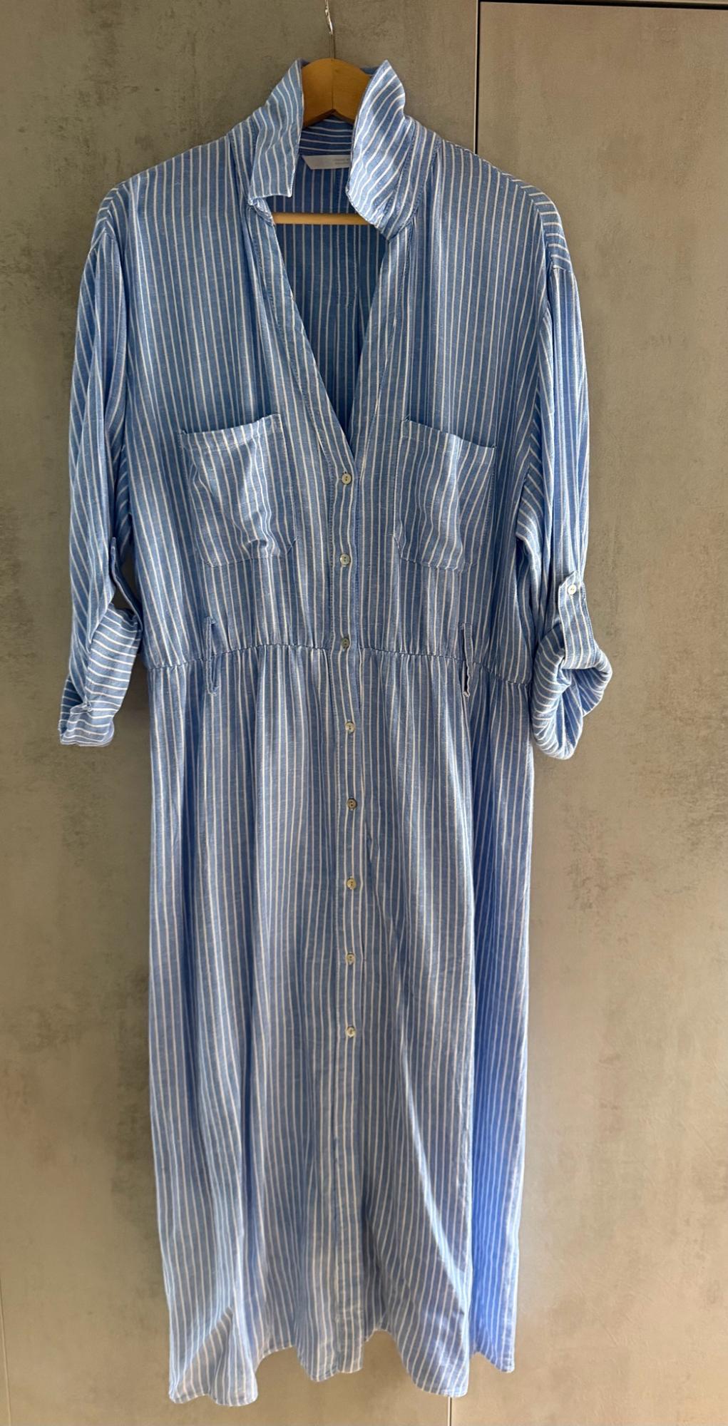 Blue and white striped shirt dress with front buttons, pockets and rolled-up sleeves, hanging on a hanger against a neutral background.