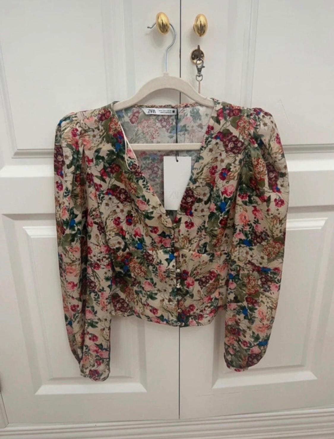 ZARA floral print blouse with a V-neck and puffed sleeves, hanging on a hanger on a white door with gold handles.