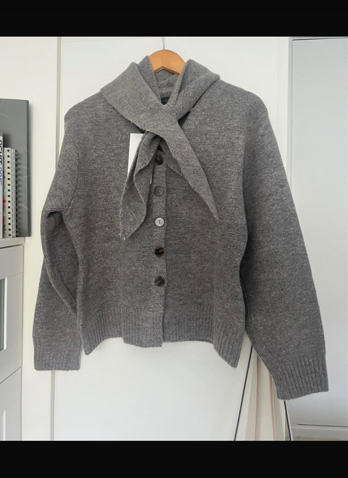 Grey wool cardigan with buttons and matching scarf, hanging on a wooden hanger against a white background.