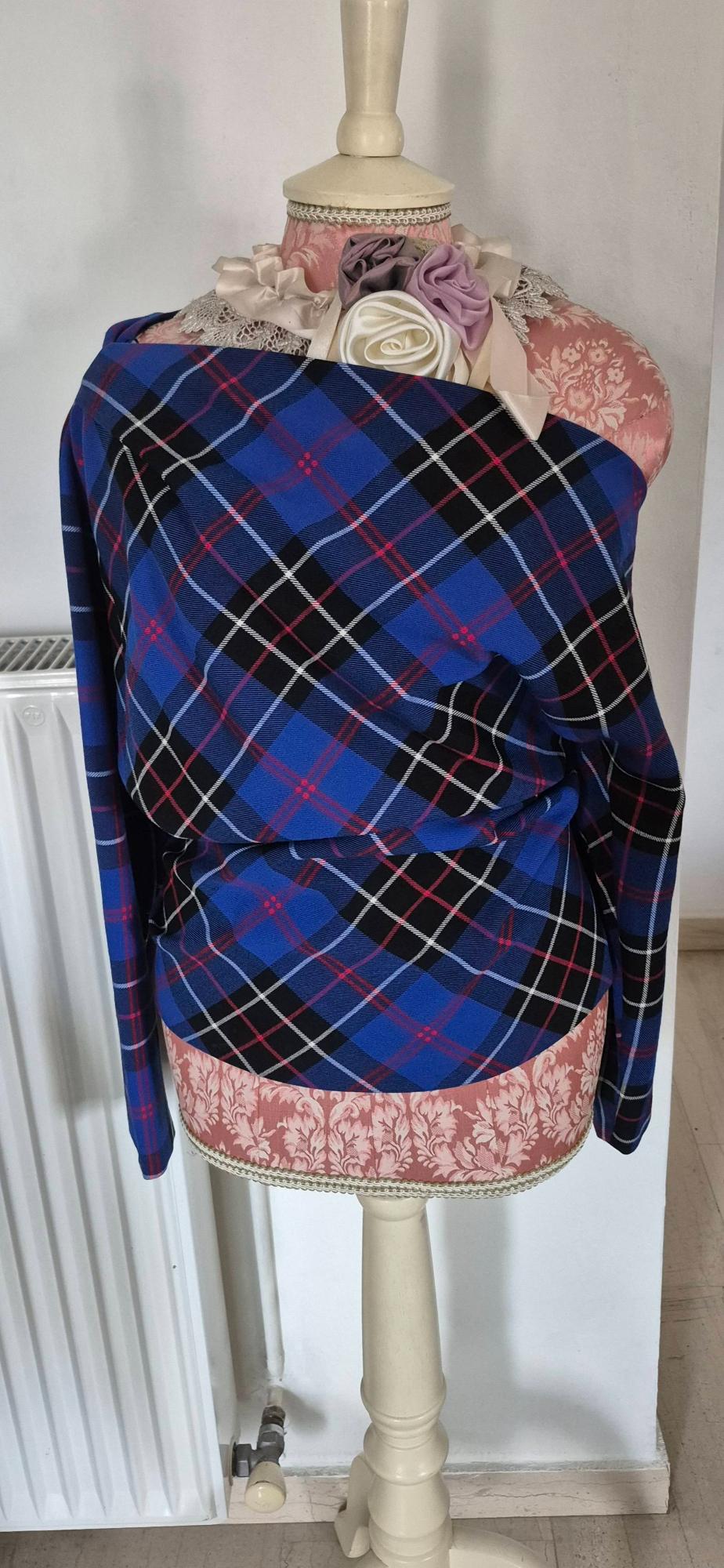 Mannequin with blue and black checked fabric, pink floral details and white lace, in a minimalist indoor setting.