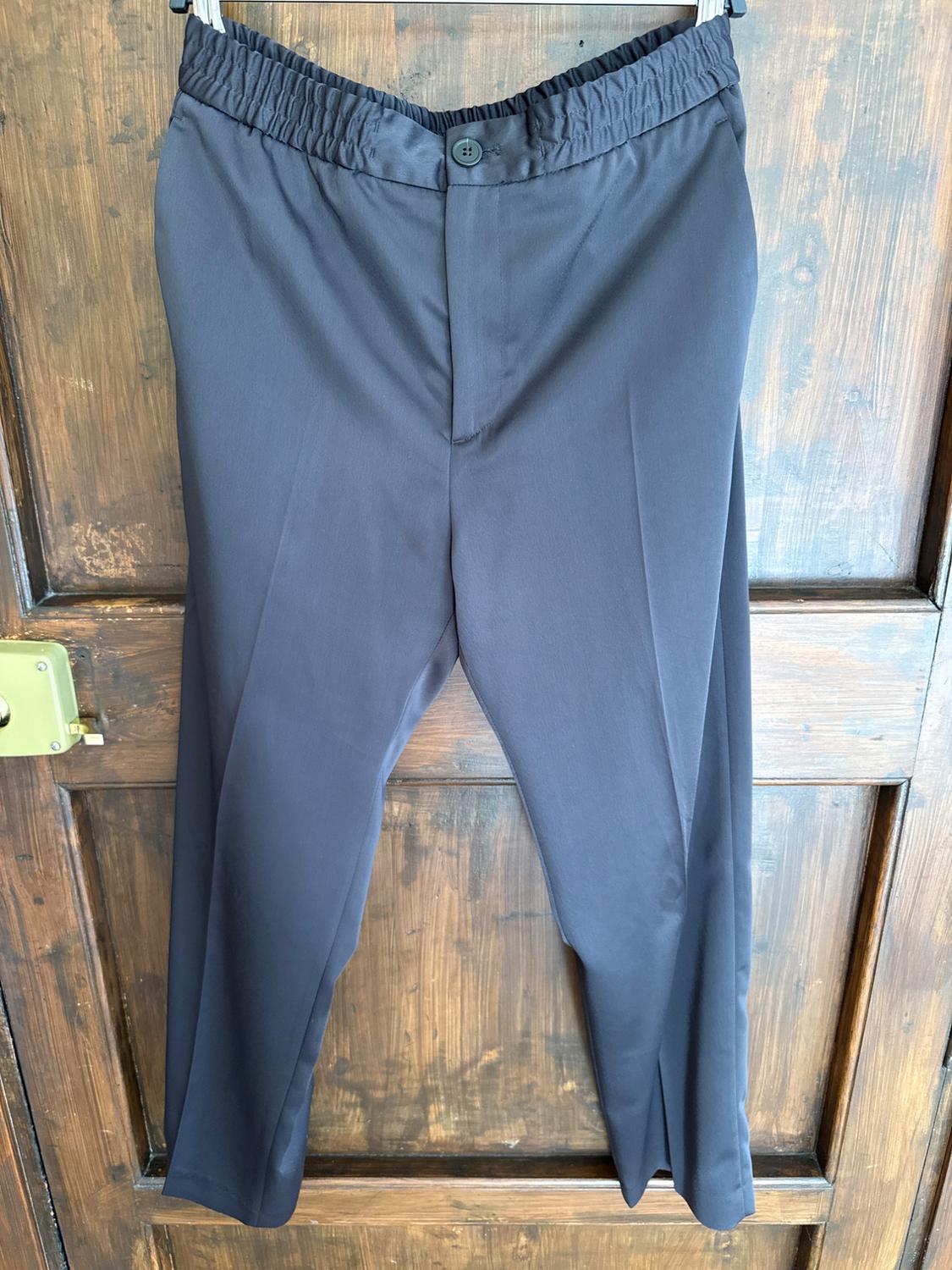 Dark grey trousers with an elasticated waist and button, hanging over a wooden door.