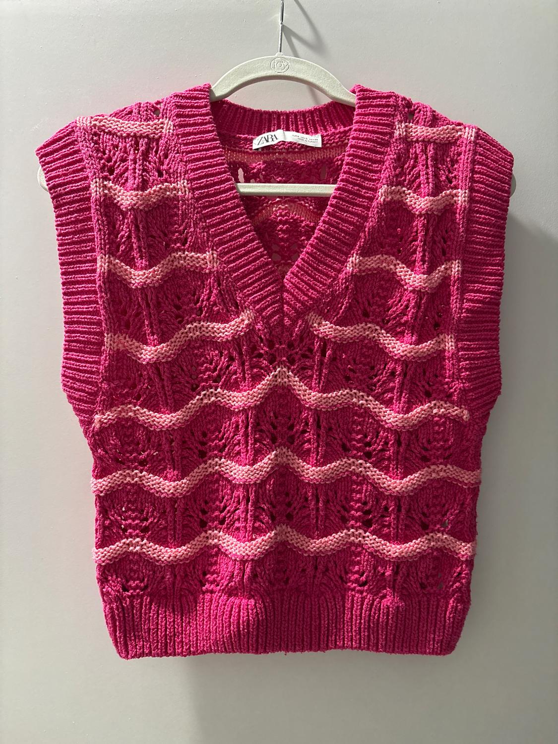 Pink knit vest with wave pattern and V-neck, hanging on a white hanger. Visible label with text "ZARA".