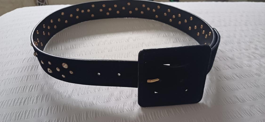 Black belt with a large square buckle and gold stud detailing on a textured white surface.