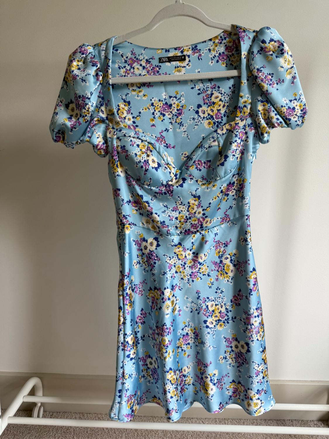 Light blue dress with a floral print in shades of yellow, purple, and white, puff sleeves, hanging on a white clothes hanger.