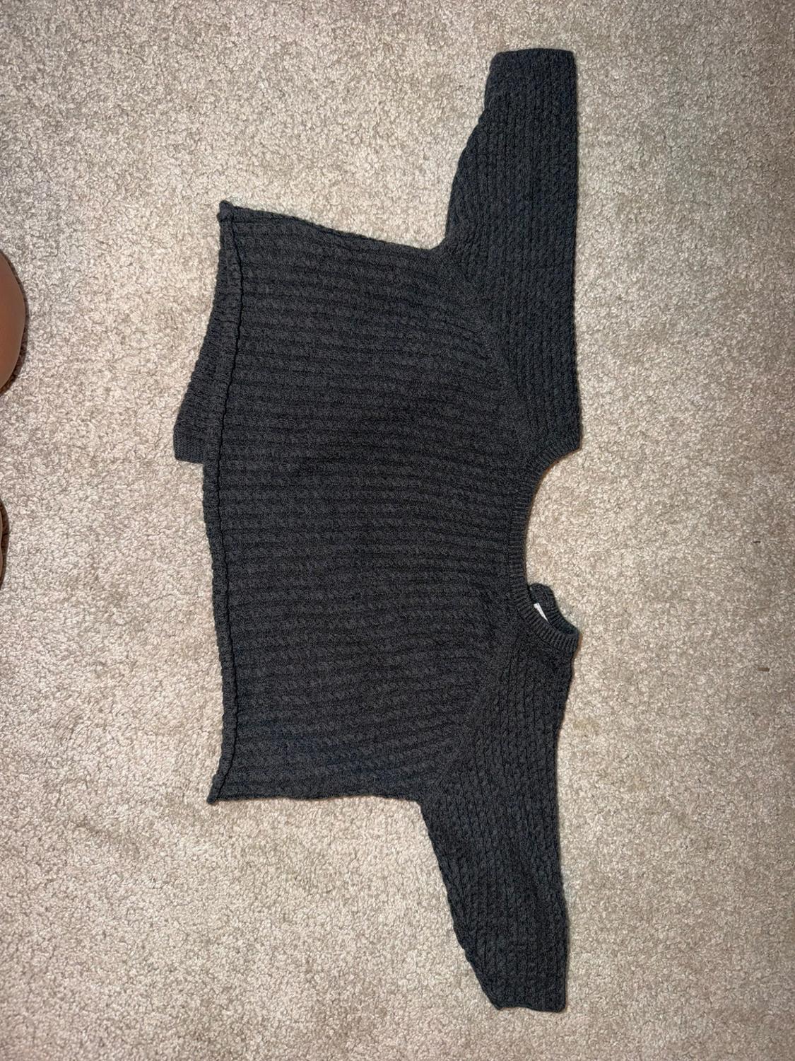 Dark grey textured knit jumper, long-sleeved with a crew neck, laid out on a beige carpet. Casual and relaxed style.