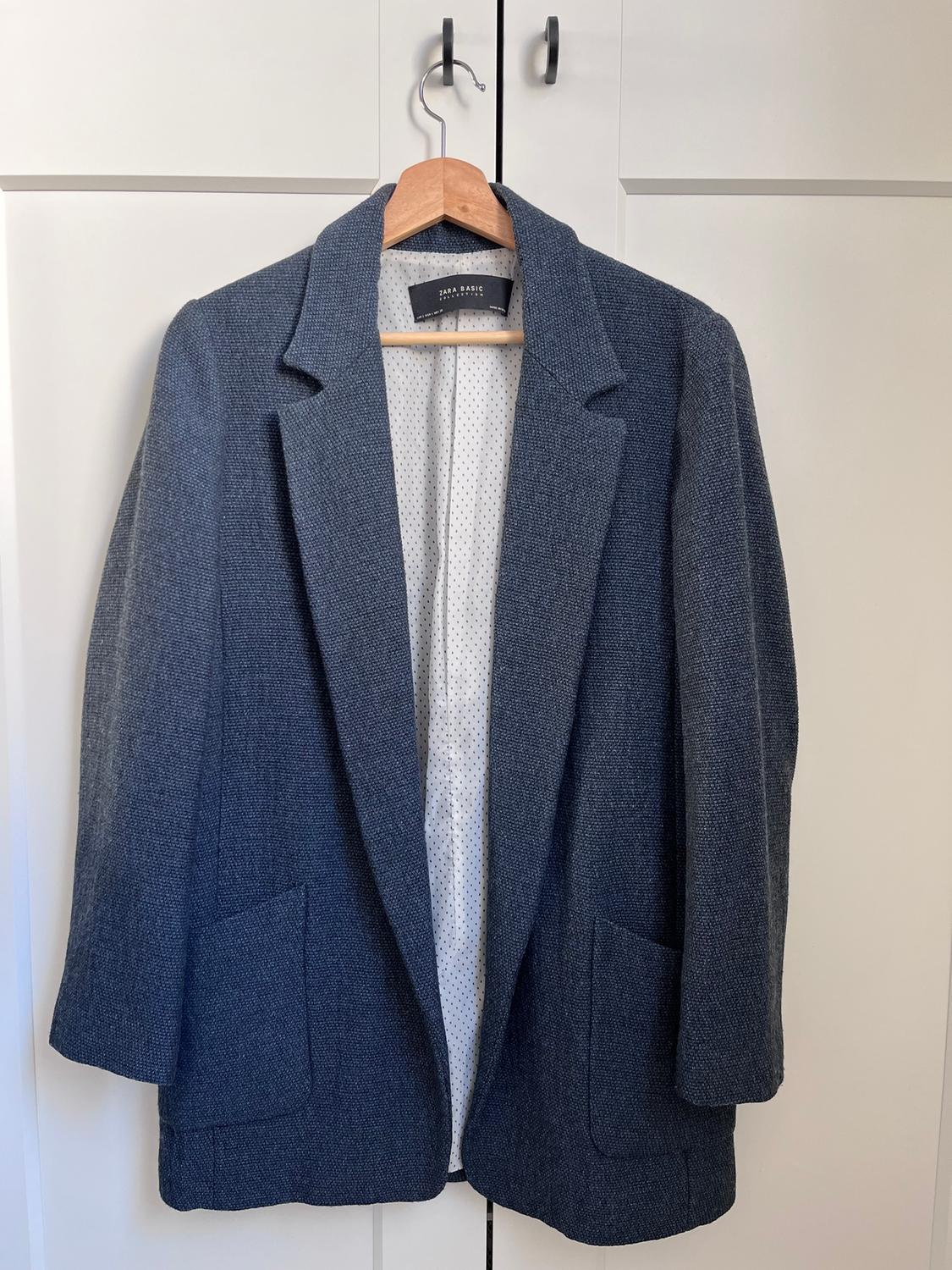 Blue jacket hanging on a wooden hanger in front of a white wardrobe. Visible label: "Zara Basic". White polka dot lining.