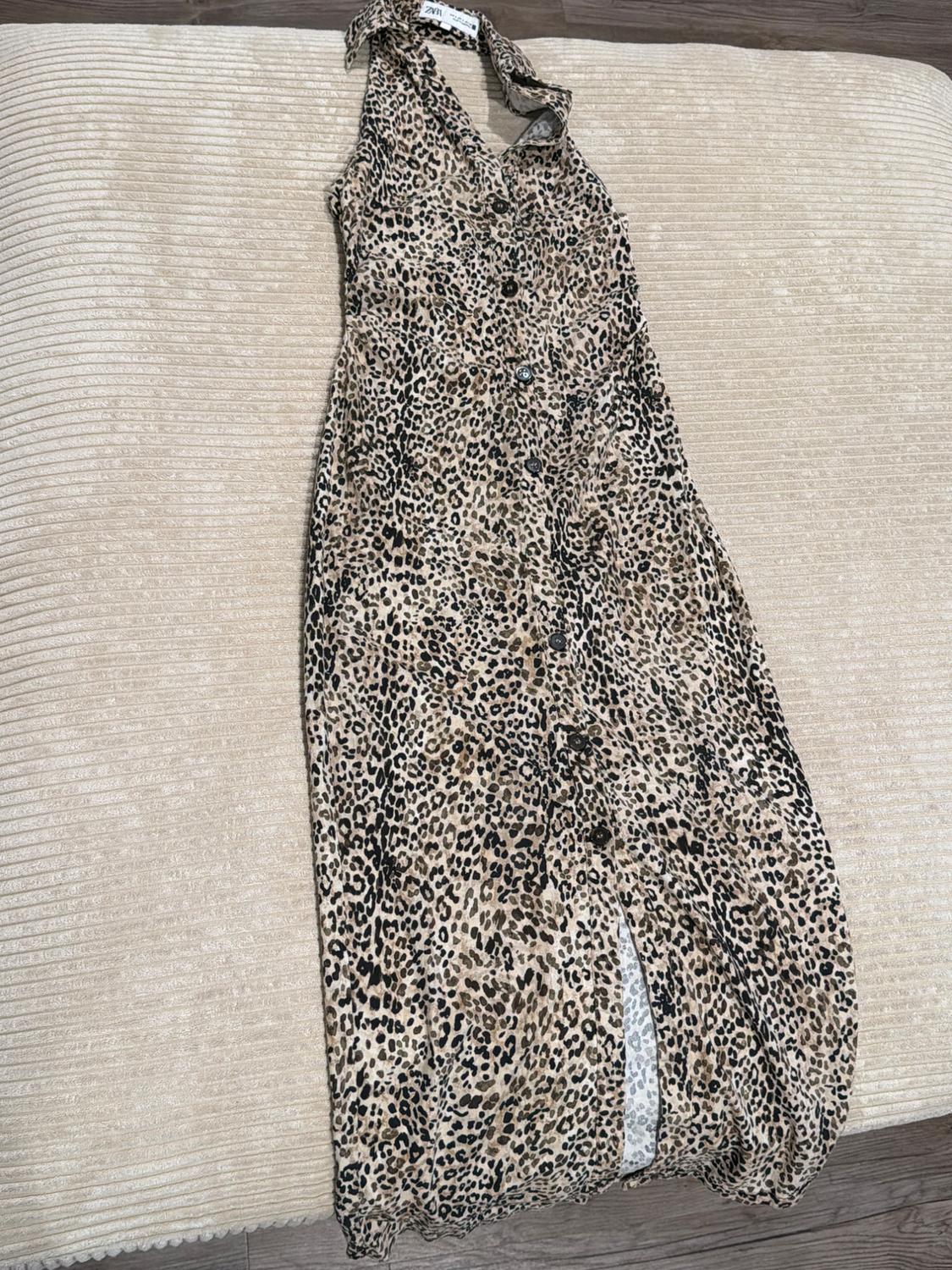 Sleeveless dress with a leopard print and front buttons, laid out on a light textured surface.