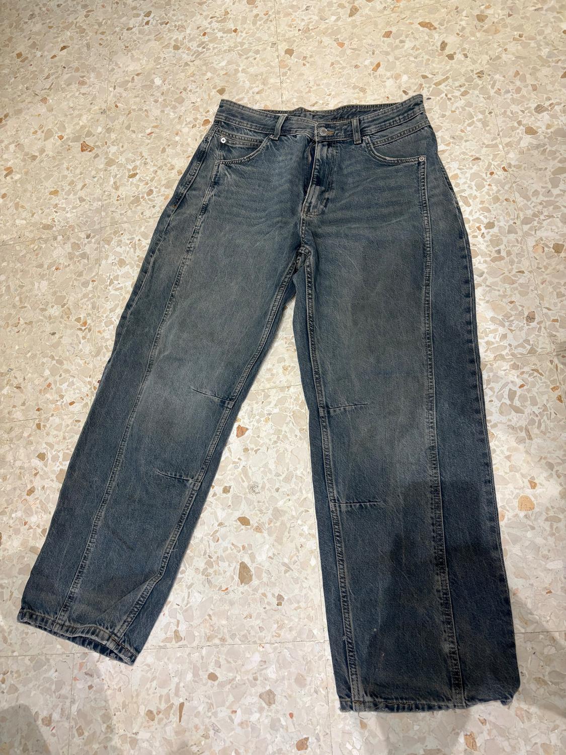 Dark, straight-cut jeans on a light tiled floor with a speckled pattern.