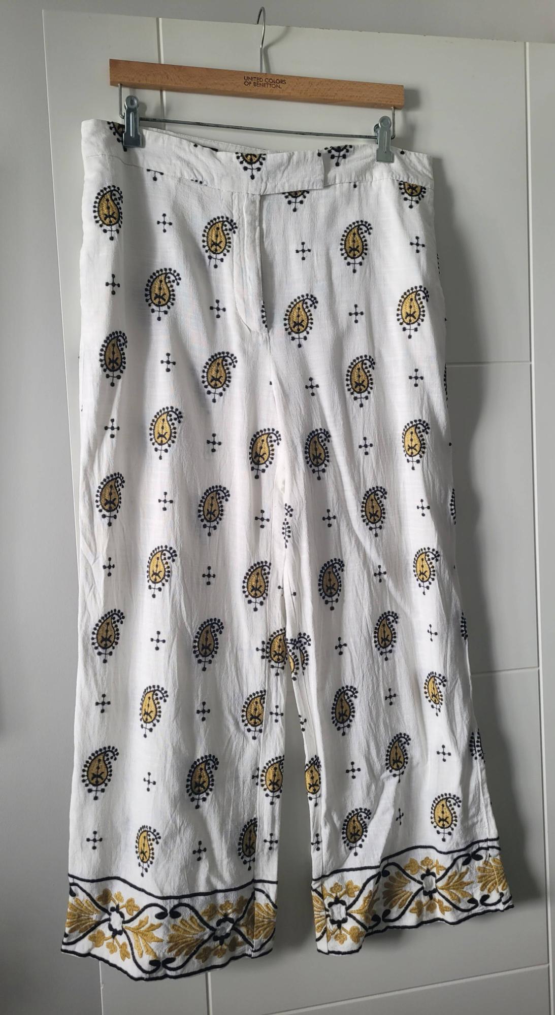 White trousers with a yellow and black paisley print, hanging on a wooden hanger from United Colors of Benetton.