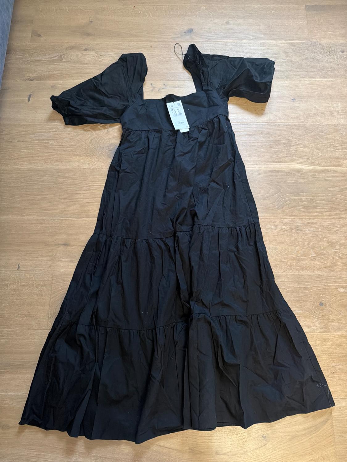 Black short-sleeved dress with visible tag, placed on a light wooden floor.
