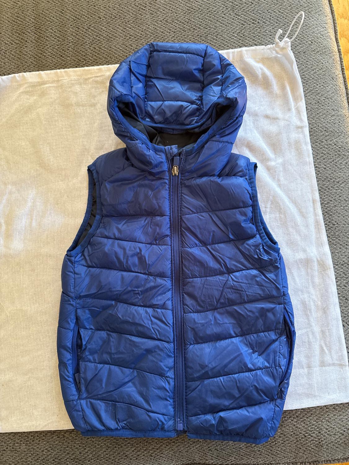 Blue padded gilet with a hood on a white fabric and grey background.