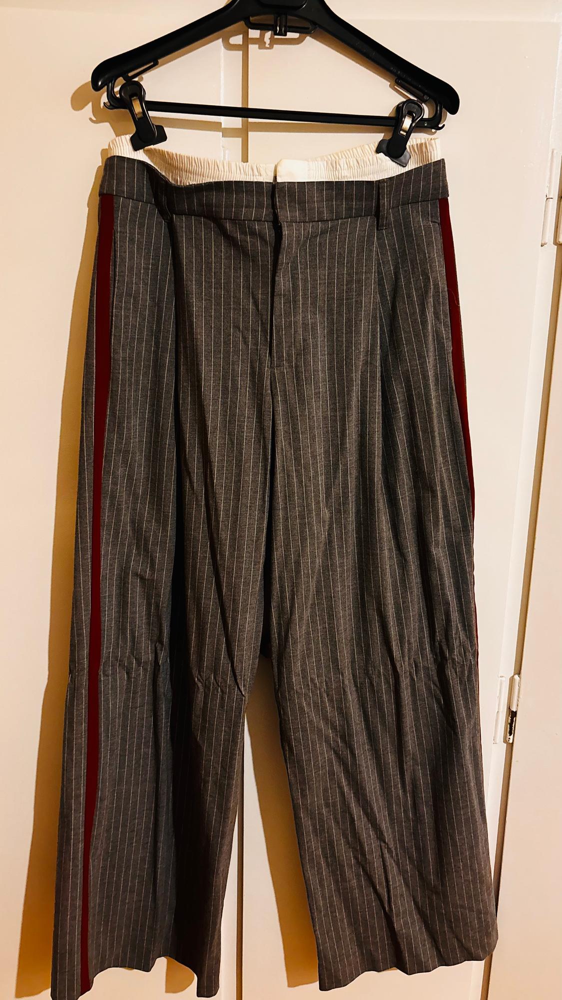 Grey trousers with white vertical stripes and a red side stripe, hanging on a black hanger over a white door.