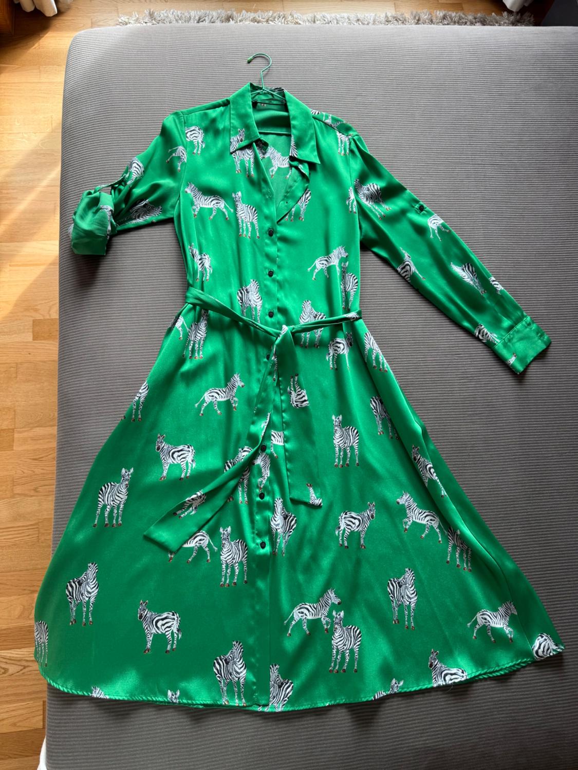 Satin green dress with black and white zebra print, long sleeves and belt, on a grey bed.