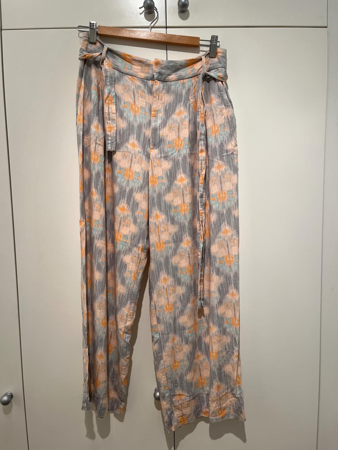 Trousers hung on a hanger, with an abstract print in grey, orange, and blue tones, against a white wardrobe background.
