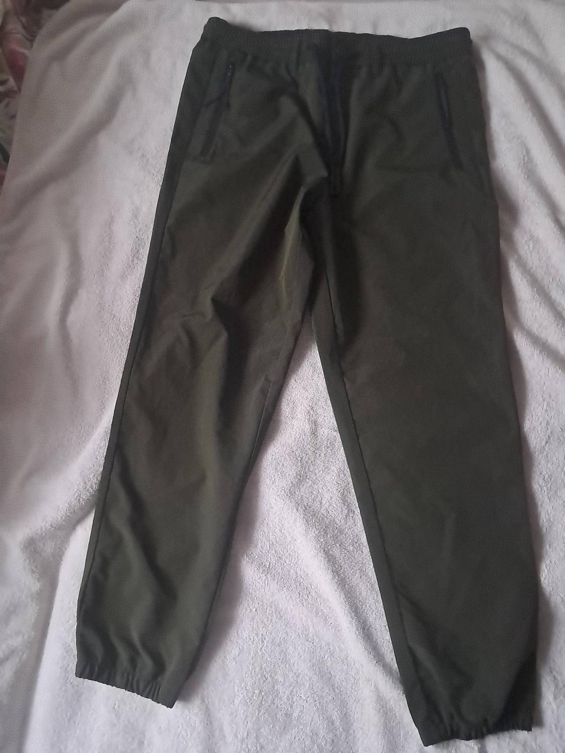 Dark green tracksuit bottoms with an elasticated waist, drawstring, zipped pockets and elasticated cuffs, on a white surface.
