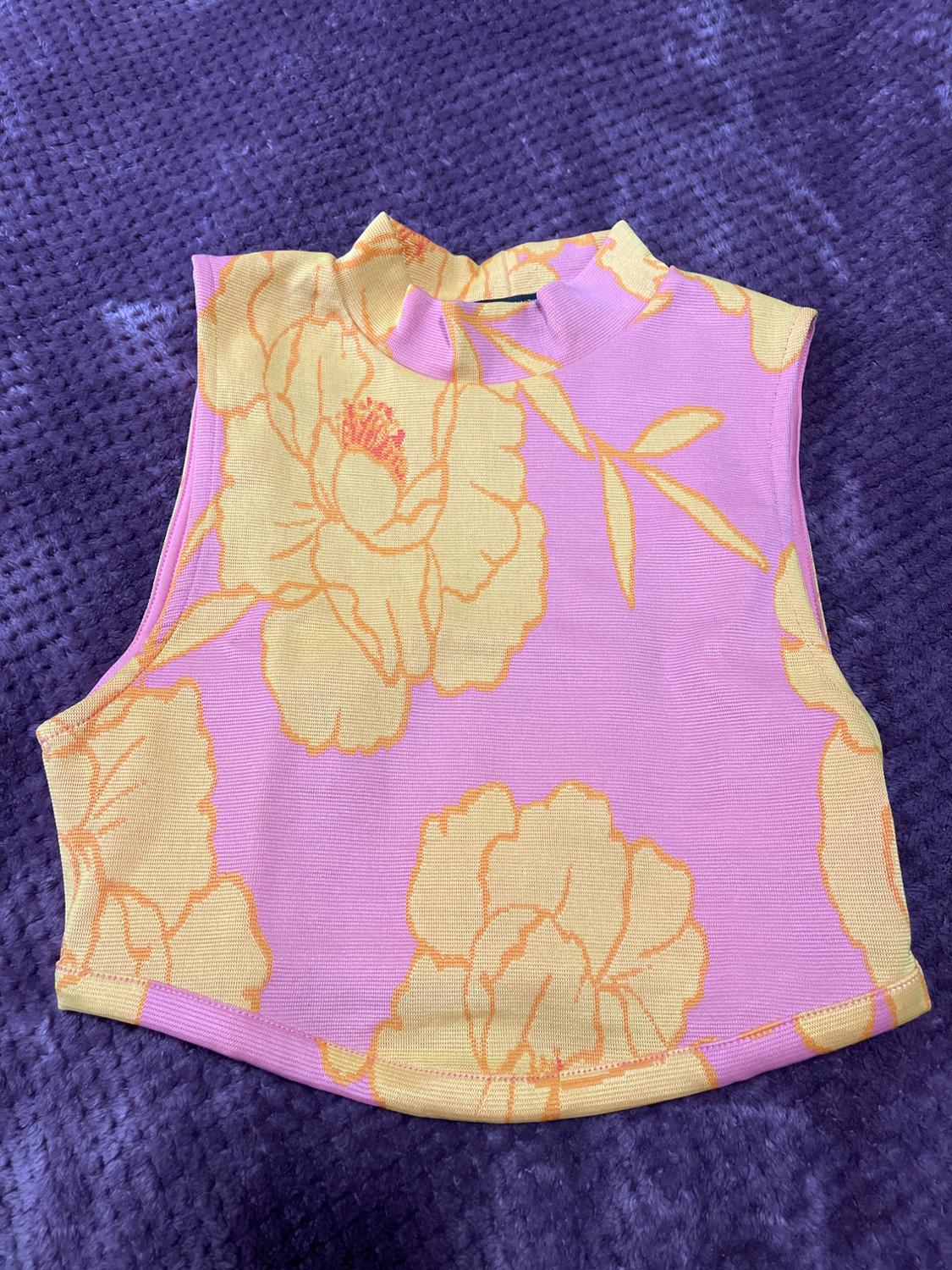 Pink sleeveless top with yellow floral print on a textured purple background.